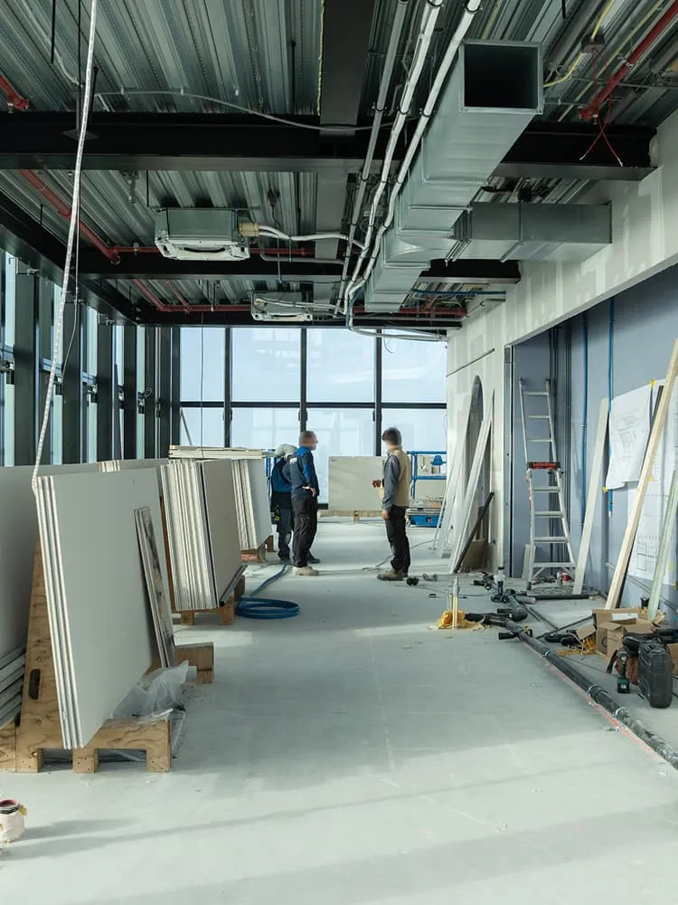 Kantoorruimte in afbouwfase met zichtbare luchtkanalen, gipsplaten en installatiewerk.