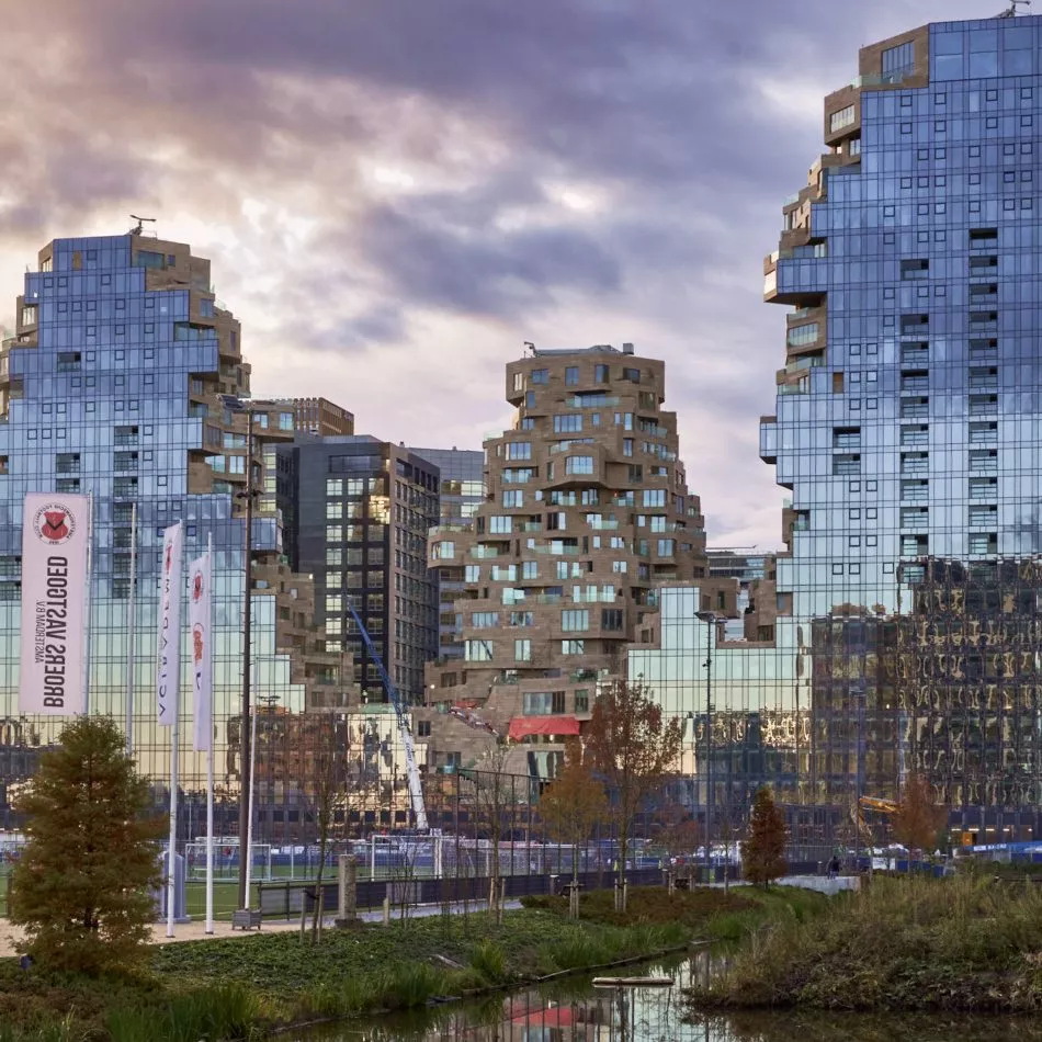 Asymmetrische hoogbouw met glanzende glazen gevels die de omgeving weerspiegelen.